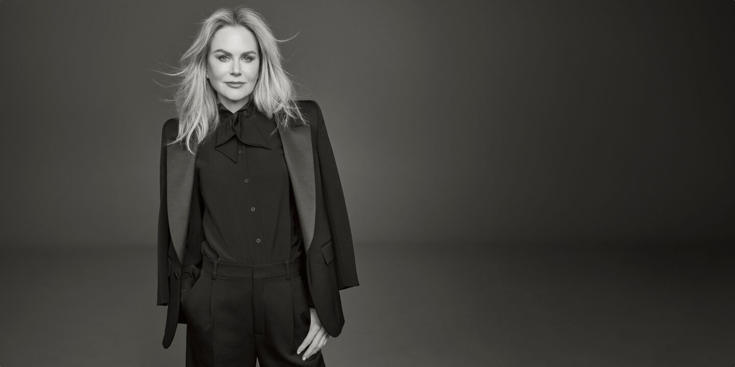 Photo of Clé de Peau Beauté’s new global brand ambassador, Nicole Kidman, wearing a black suit with right hand in pocket, looking directly at the camera in a monochrome image.