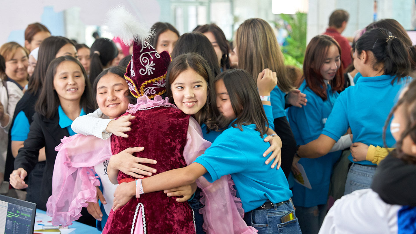 Photo of a woman in a UNICEF blue shirt hugging a girl in traditional Kyrgyz attire.