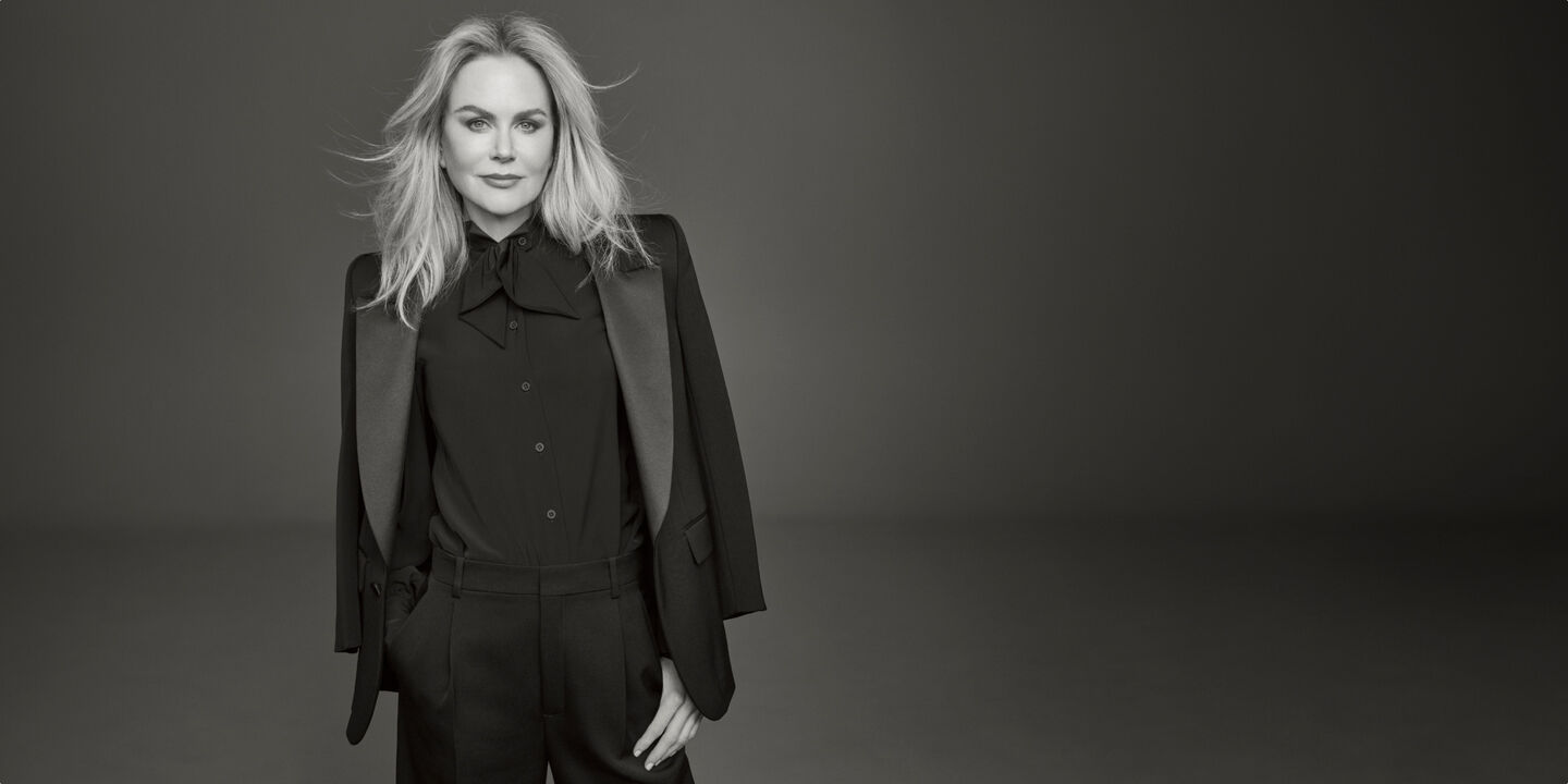 Photo of Clé de Peau Beauté’s new global brand ambassador, Nicole Kidman, wearing a black suit with right hand in pocket, looking directly at the camera in a monochrome image.