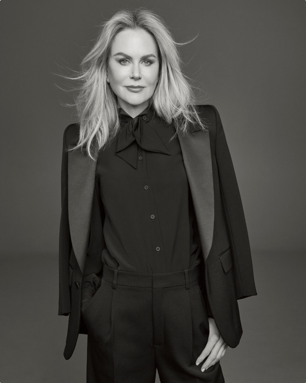 Photo of Clé de Peau Beauté’s new global brand ambassador, Nicole Kidman, wearing a black suit with right hand in pocket, looking directly at the camera in a monochrome image.