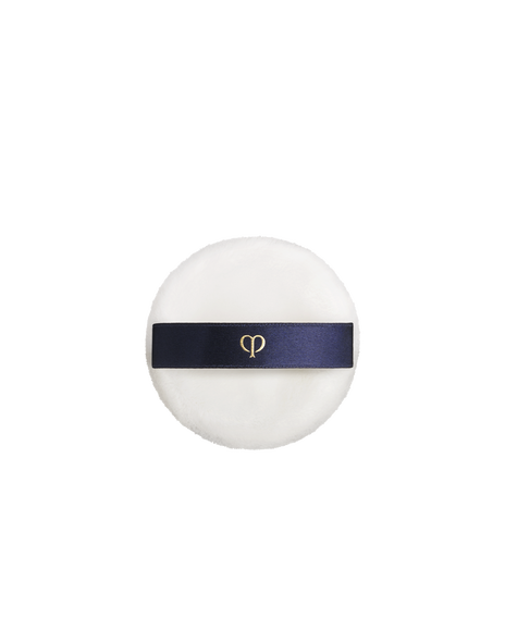 Photo of a soft, round white powder puff with a navy satin band featuring a gold logo.
