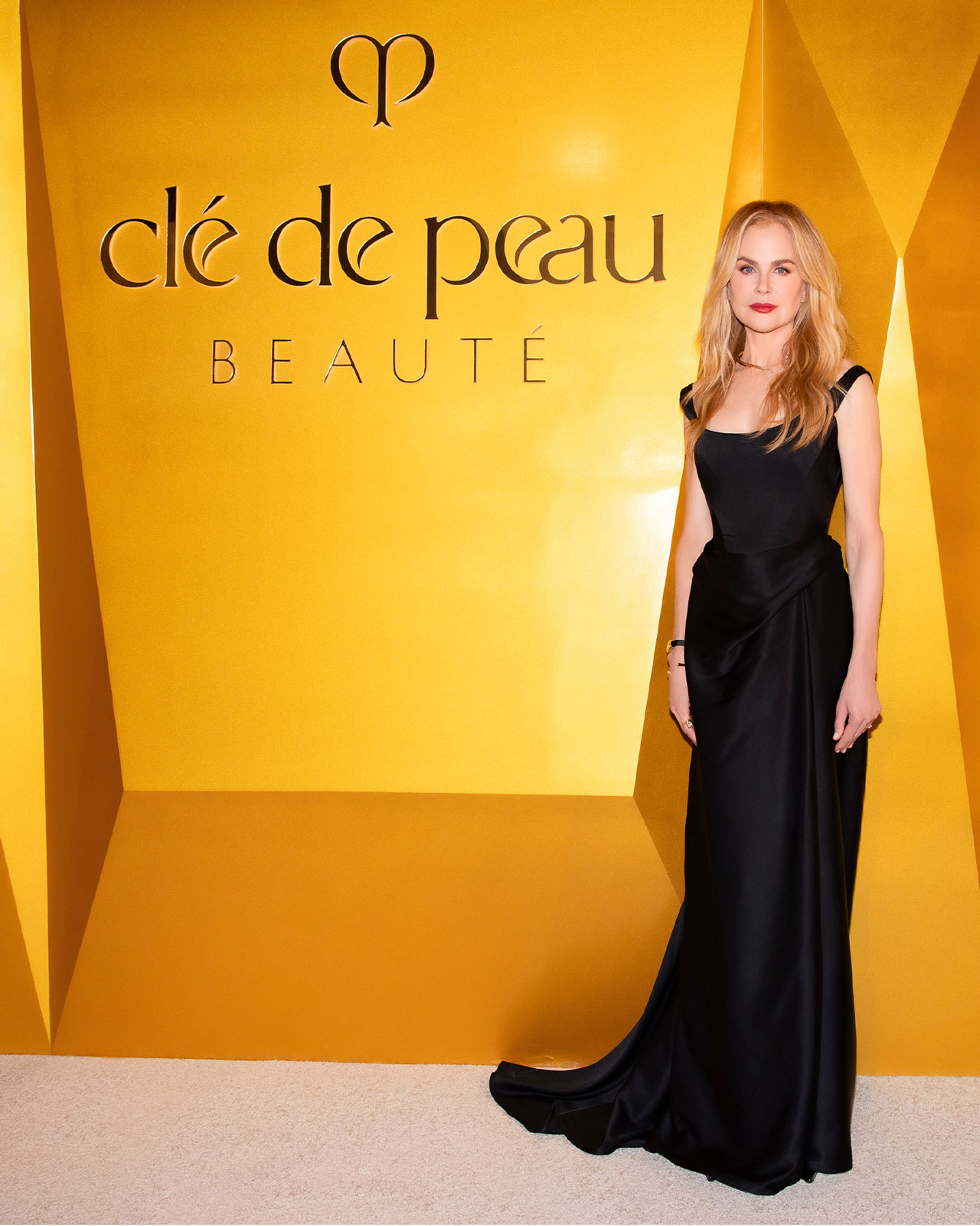 Photo of Nicole Kidman, Global Brand Ambassador for Clé de Peau Beauté, poses elegantly in a black dress at a Los Angeles event. She stands before a golden display featuring the brand's iconic La Crème.