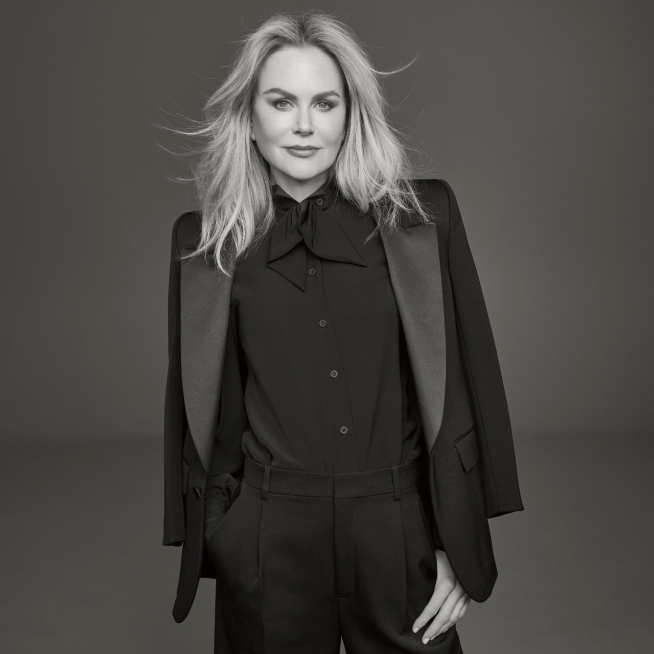 Photo of Clé de Peau Beauté’s new global brand ambassador, Nicole Kidman, wearing a black suit with right hand in pocket, looking directly at the camera in a monochrome image.