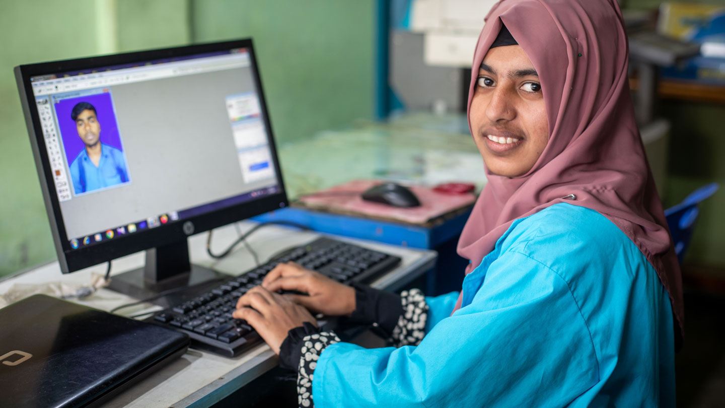 Photo of a girl in the Alternative Learning Program smiling at the camera while working at a computer in a training center.